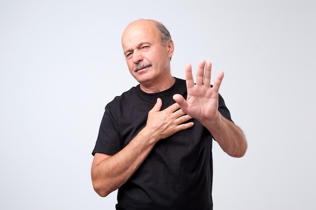 Displeased mature man refusing stretching hands to camera over grey background