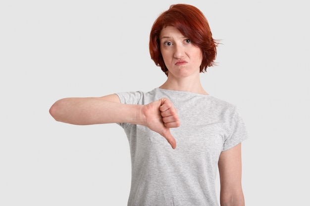 Displeased red haired woman keeps thumb down