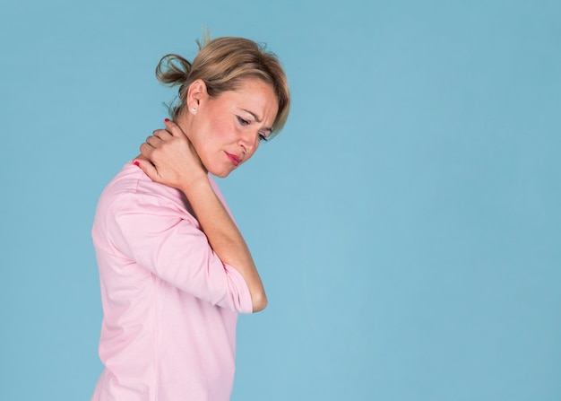 Displeased woman suffering from neck pain on blue background