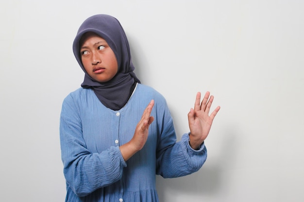 Displeased young Asian girl in hijab making stop gesture isolated on white background