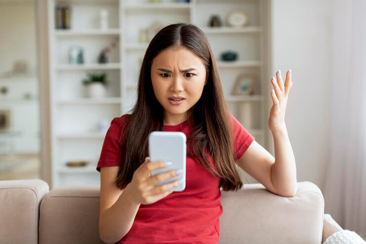家でスマートフォンの画面を見ている不満の若いアジア人女性