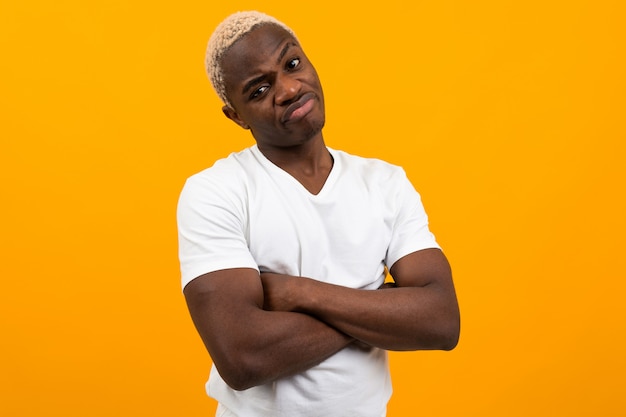 Displeased young black african man in white t-shirt posing on yellow isolated with copy space