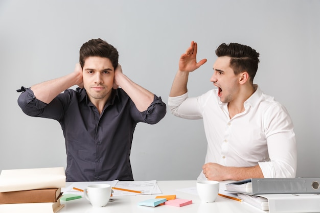 Displeased young business man covering ears because of his colleague