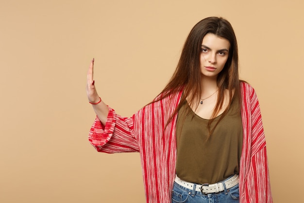 Displeased young woman in casual clothes looking camera, showing stop gesture with palm aside isolated on pastel beige wall background. People sincere emotions, lifestyle concept. Mock up copy space.