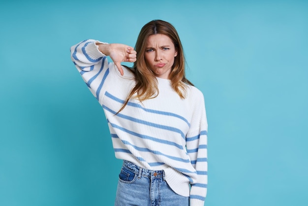 Displeased young woman showing her thumb down while standing against pink background