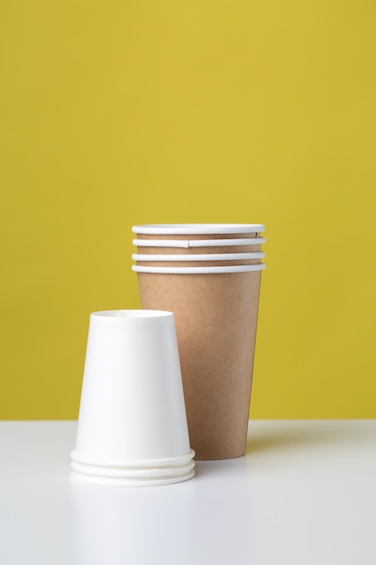 Disposable cardboard biodegradable glass on a white table yellow background