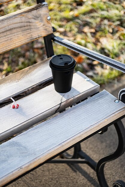 凍った朝の公園のベンチで使い捨てのコーヒー カップ