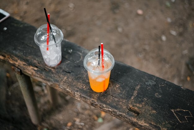 ベンチにフレッシュジュースと氷が入った使い捨てカップ。暑い夏のさわやかな冷たい飲み物。