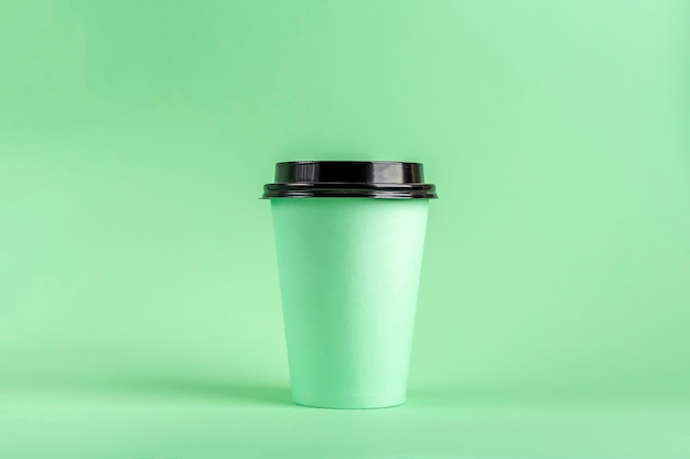 Disposable Eco Paper Cup with coffee on green background. Mockup for advertising.