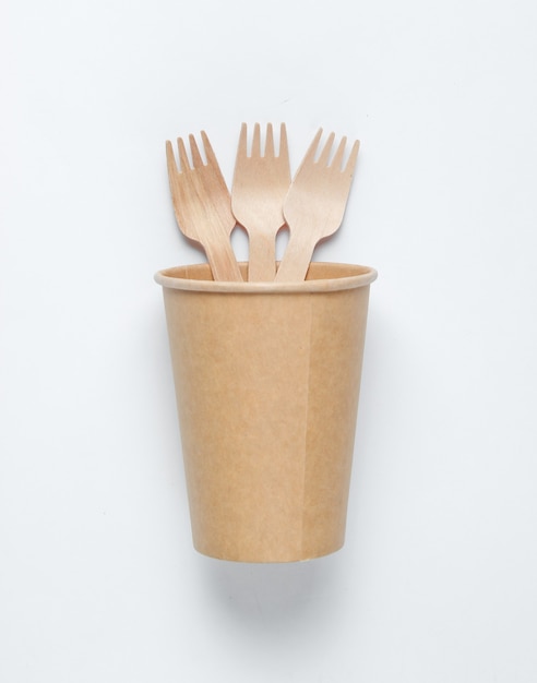 Disposable empty coffee cup with forks of natural materials on white background. Eco friendly concept.