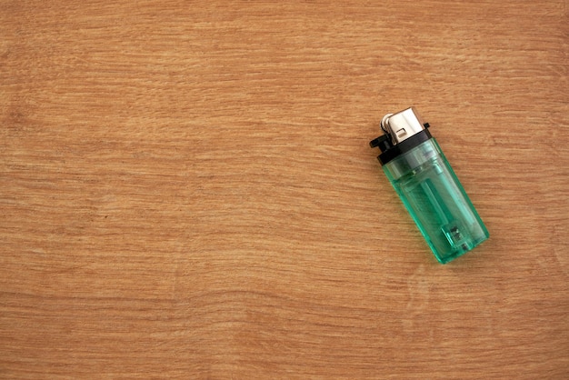 Disposable green lighter on a wooden table.