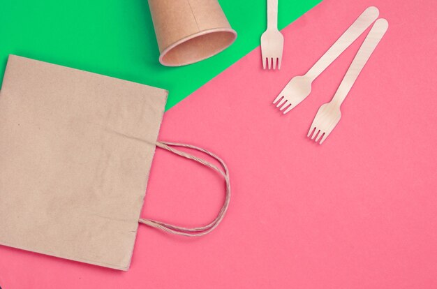 Disposable kitchenware of natural materials. Eco friendly concept. Wooden forks, empty craft coffee cup, bag on green pink