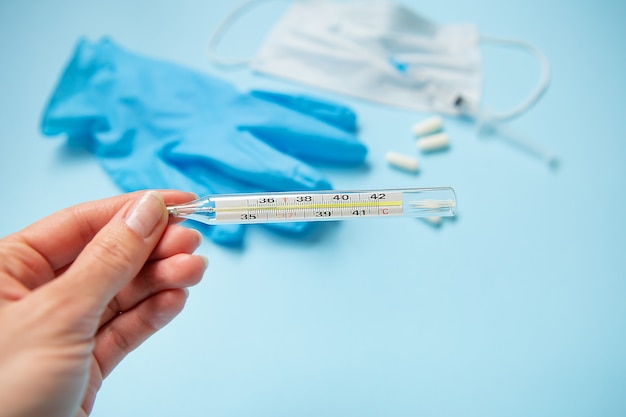 Disposable medical face mask closes the mouth and nose, on a blue background with pills and a thermometer.