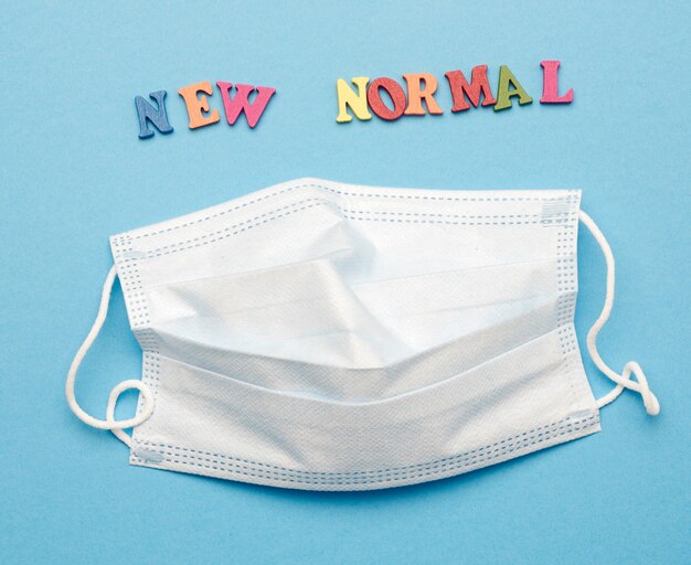 Disposable medical face mask and lettering new normal on blue