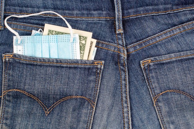 Photo disposable medical protective surgical mask and  american dollars banknotes peeking in jeans  pocket