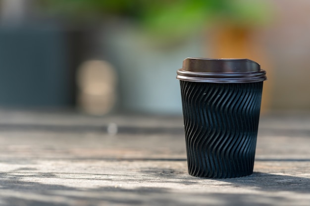 Disposable paper coffee mug is placed on the wooden table for takeaway