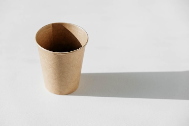 Disposable paper cup with shadow from light on a white background. Copy, empty space for text