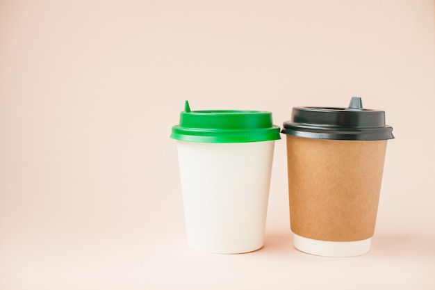 Disposable paper cups with a plastic lid on a light pink background.