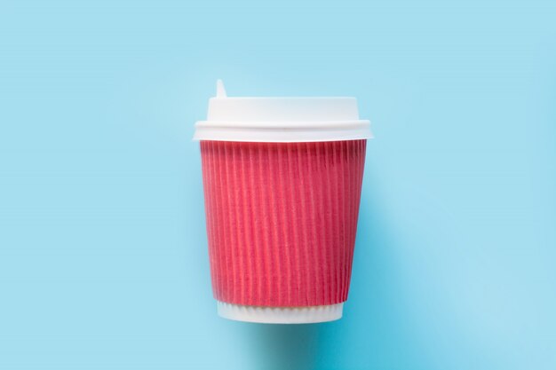 Photo disposable paper red cup with a white plastic lid for hot coffee or tea on blue.