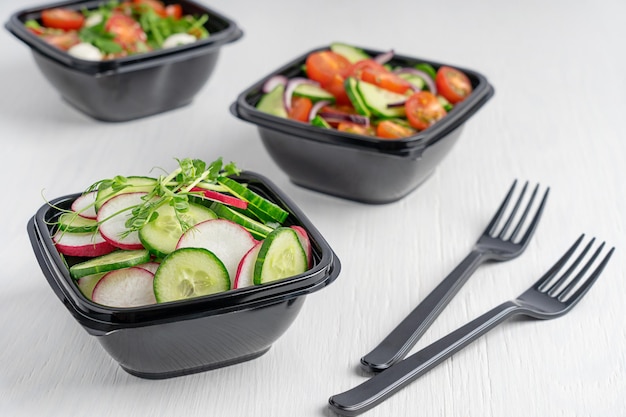 Одноразовые пластиковые ланч-боксы, используемые для доставки еды с различными овощными салатами на столе