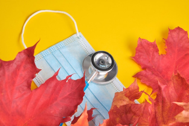 일회용 보호 의료 마스크와 청진기, 가을 단풍잎은 노란색 배경 복사 위치, 계절 감기 개념, 코로나바이러스 2020 대유행