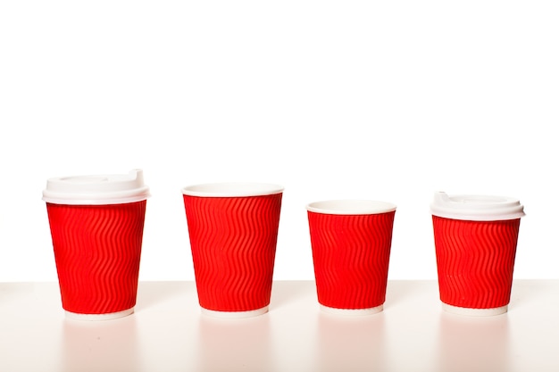 Одноразовые красные бумажные кофейные чашки разных размеров, стоящие в ряд на белом фоне, макет для дизайна для эспрессо, капучино, латте