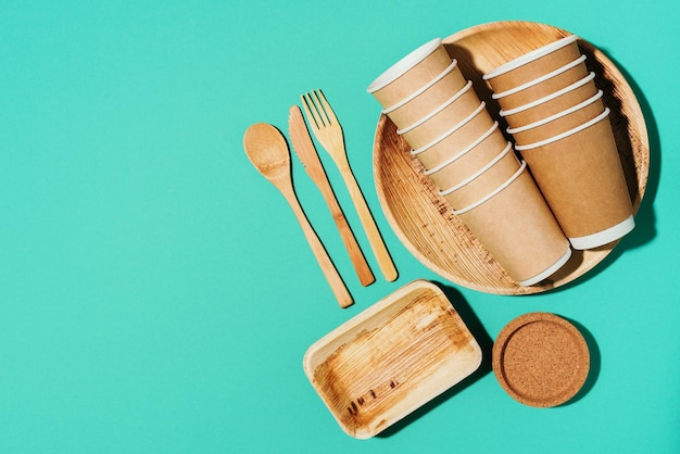 Disposable tableware from natural materials Bamboo plates wooden spoon fork knife craft paper cups on blue background Ecofriendly sustainable lifestyle Ecofriendly disposable utensils