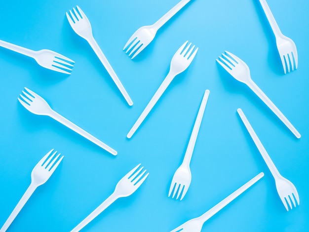 Disposable tableware, white plastic forks scattered on a blue background, top view, flat lay.