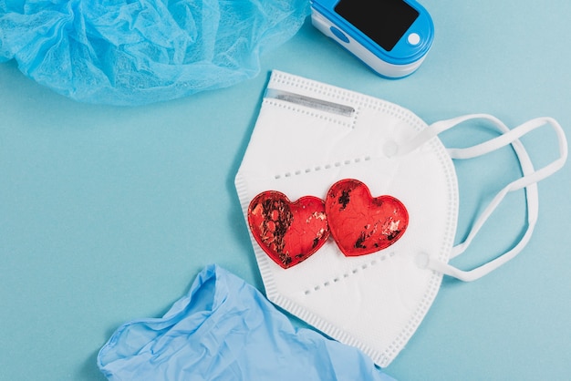 Disposable white medical mask, oximeter on blue background, top view