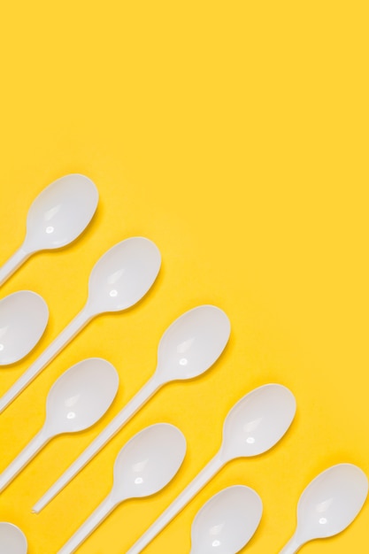 Disposable white plastic spoons on a yellow background in a top view