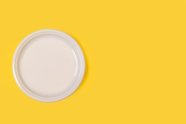 A disposable white plate on a yellow background with copy space