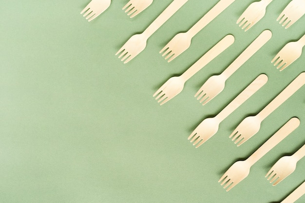 Disposable wooden forks top view on green surface with copy space