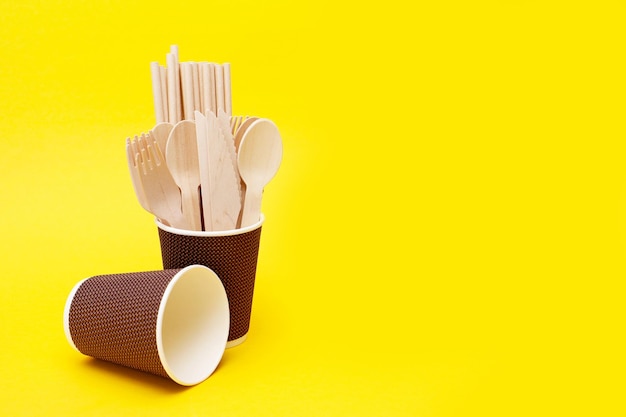 одноразовые деревянные ложки вилки и ножи в бумажной чашке на желтом фоне с переработанным копировальным пространством