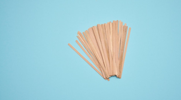 Disposable wooden sticks for stirring hot drinks on a blue background Coffee and tea spoon zero waste