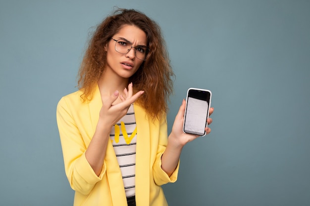 Dissatisfied angry attractive young woman with curly dark blond hair wearing yellow jacket and