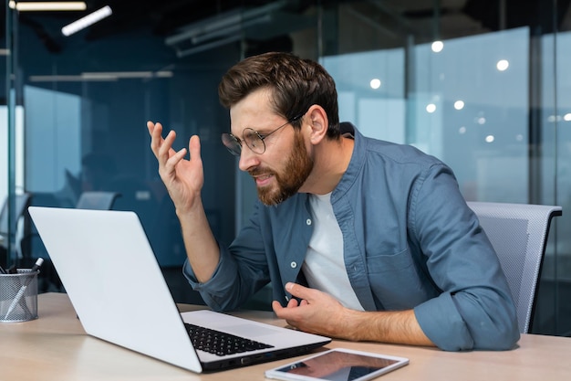 Dissatisfied and angry businessman looking at laptop screen man in casual shirt working inside