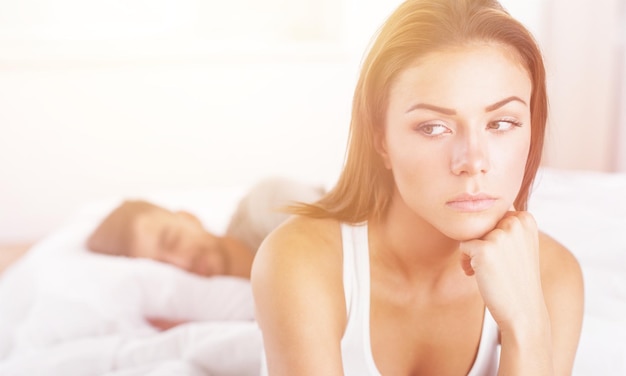 Dissatisfied beautiful young woman in bed with sad expression on her face,