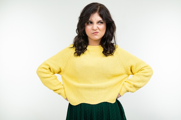 Dissatisfied girl in a yellow sweater and green skirt on a white background