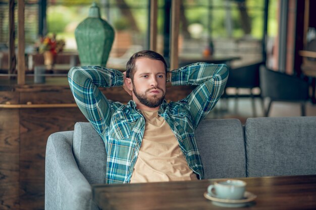 夏のカフェでの長い待ち時間に疲れた頭の後ろで手を上げる不満の男