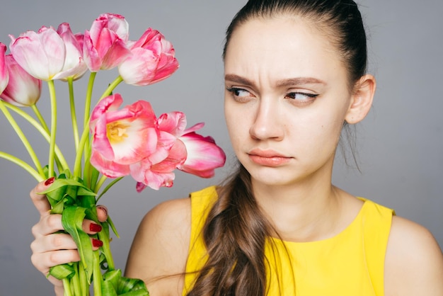 Dissatisfied sad girl in a yellow dress holds pink flowers and looks at them