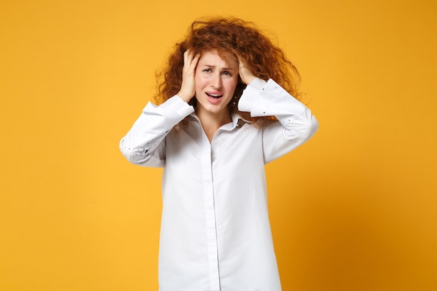 Dissatisfied upset young redhead woman girl in white shirt posing isolated on yellow orange wall