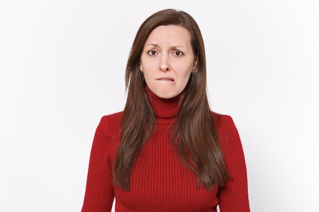 Dissatisfied worried young brunette woman girl in casual red clothes posing isolated on white background studio portrait. People sincere emotions lifestyle concept. Mock up copy space. Biting lips.