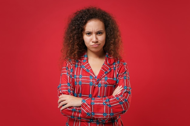 Foto giovane ragazza afroamericana insoddisfatta in pigiama homewear in posa mentre si riposa a casa isolata su sfondo rosso. rilassatevi il concetto di stile di vita di buon umore. mock up spazio di copia. tenendosi per mano incrociata.