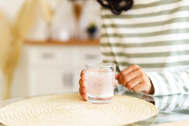 自宅で薬を服用している認識できない女性がコップ一杯の水にフィズ薬を溶かす