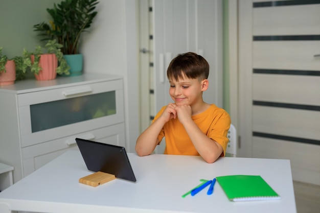 Distance education at home during quarantine child elementary\
school boy doing homework with a tablet