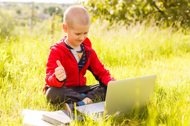 Дистанционное обучение. Мальчик учится на ноутбуке. Делать домашнее задание на траве. Ребенок учится на свежем воздухе. Руки ребенка и компьютер