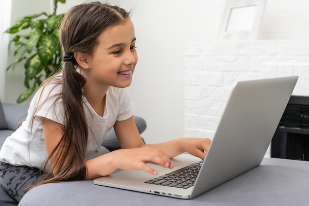 Дистанционное обучение. Веселая маленькая девочка в наушниках с помощью ноутбука учится через онлайн-систему электронного обучения.