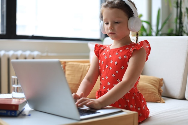 Distance learning. Cheerful little girl using laptop computer studying through online e-learning system.