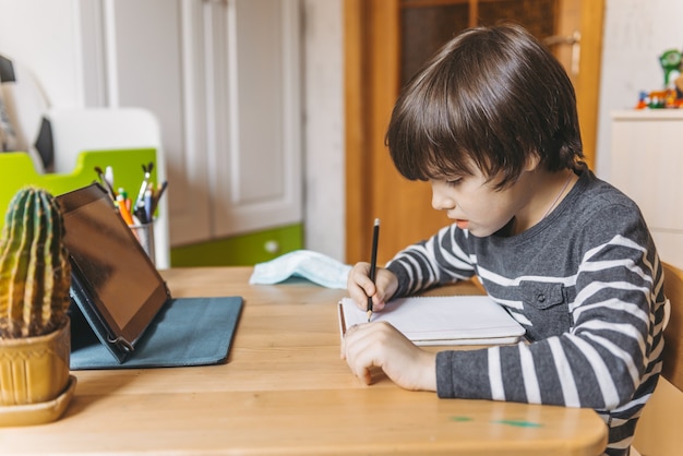 Photo distance learning for children during the coronavirus epidemic. a boy sits at a table and performs tasks of a teacher on the internet.