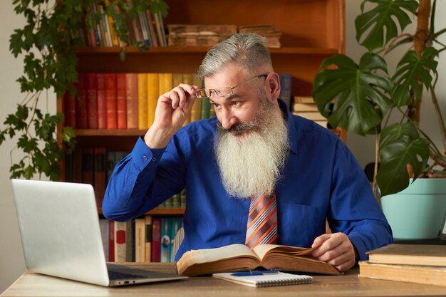 Distance Learning Concept. Teacher professor tutor teaches discipline online. Mature bearded man answers teacher's question through laptop.